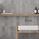 Bathroom with gray tiled walls, wooden shelf, and white sink.